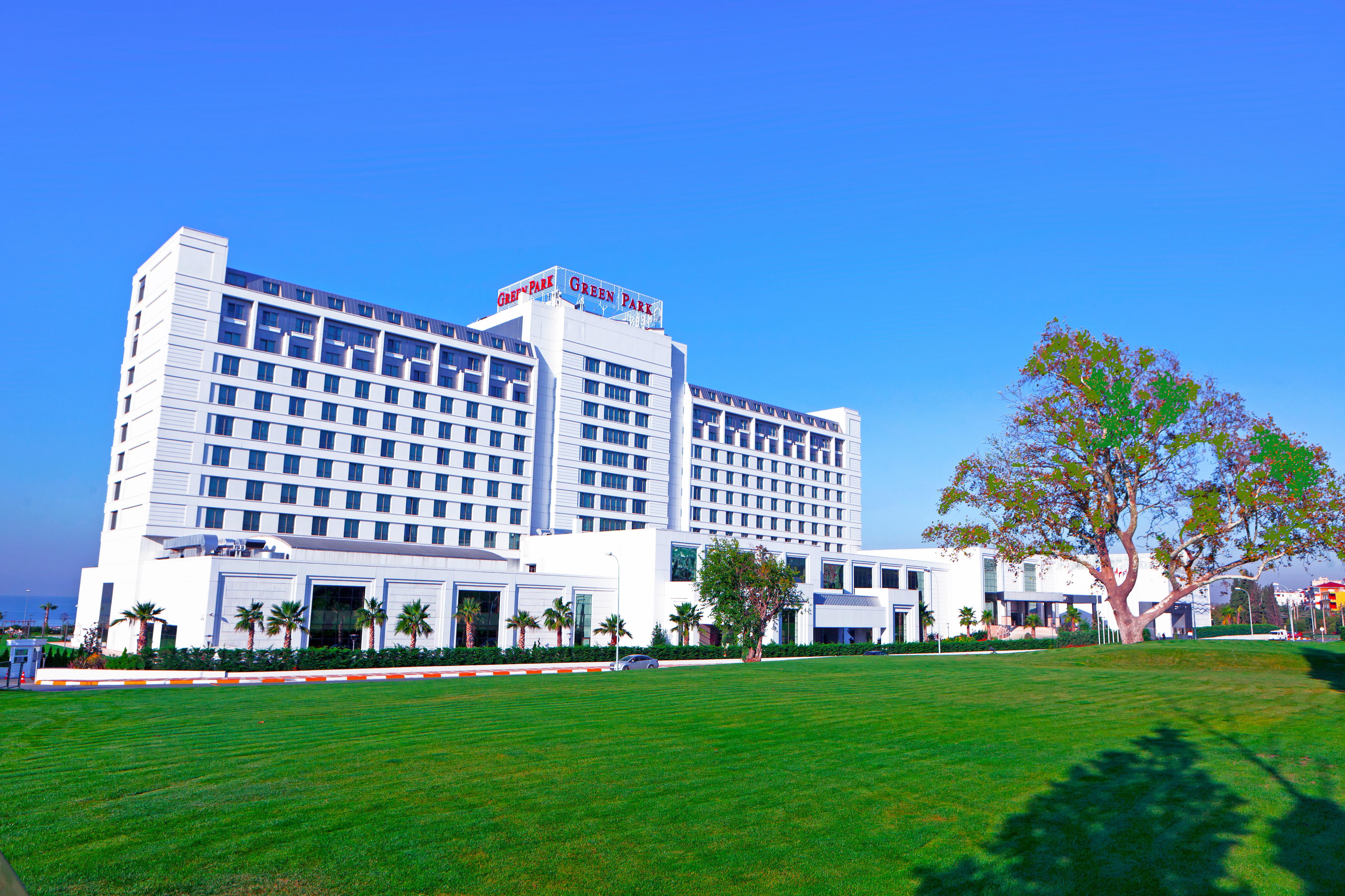 The Green Park Pendik İstanbul Dış mekan fotoğraf The photo shows a modern multi-story hotel building with a clean, contemporary design. The structure features large windows and a prominent sign at the top indicating its name. In front of the hotel, there is a well-maintained green lawn with some la